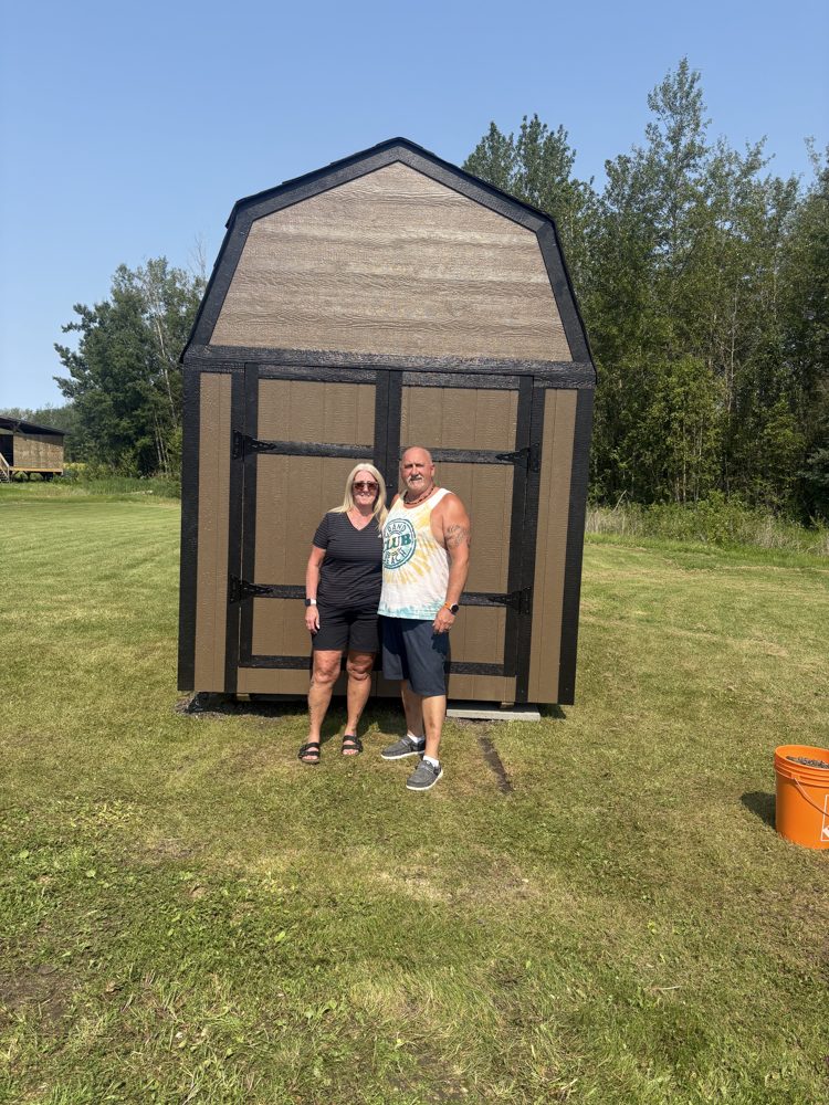 A couple in front of their new brown Apex barn shed on an acreage