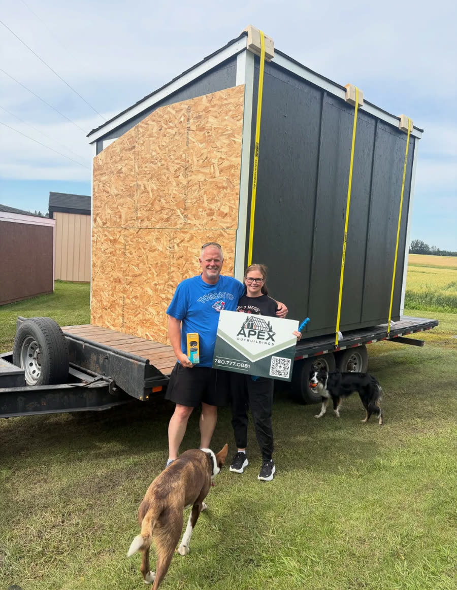 Two customers and their dogs with an Apex Outbuildings sign beside a delivered shed