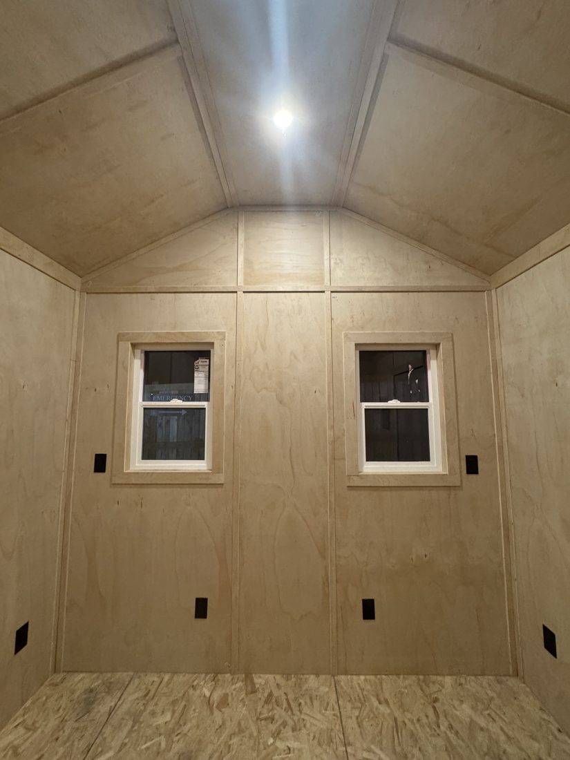 Inside an Apex building lined with plywood, with two windows and a steel door
