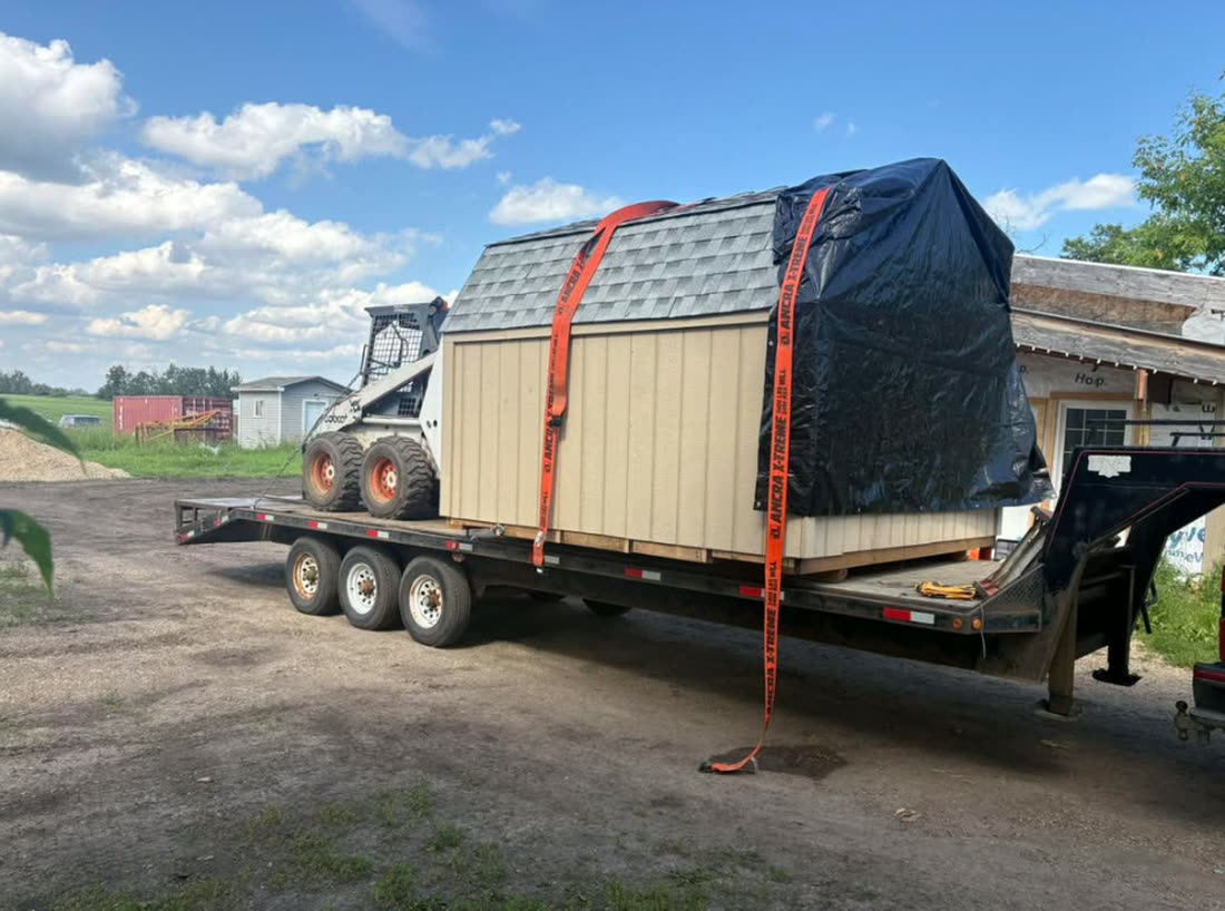 An Apex barn shed strapped to a flatbed trailer, ready to deliver